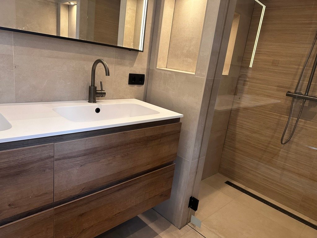 Modern eiken wastafelmeubel passend bij de houtlook tegels in een luxe badkamer.