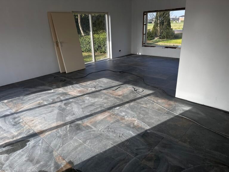 egelzetter bezig met verlijmen van grote 60x120 cm tegels op een ontkoppelde ondervloer.