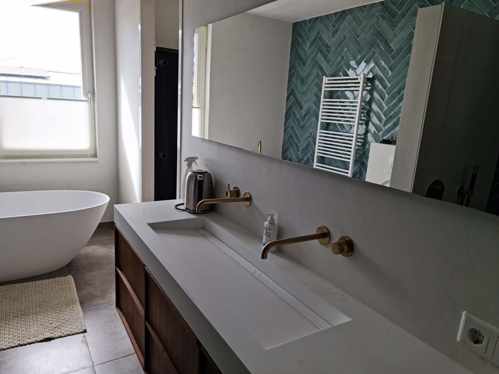 Moderne badkamer met grijze beton ciré wanden, een wit vrijstaand bad en een accentmuur in visgraatmotief.