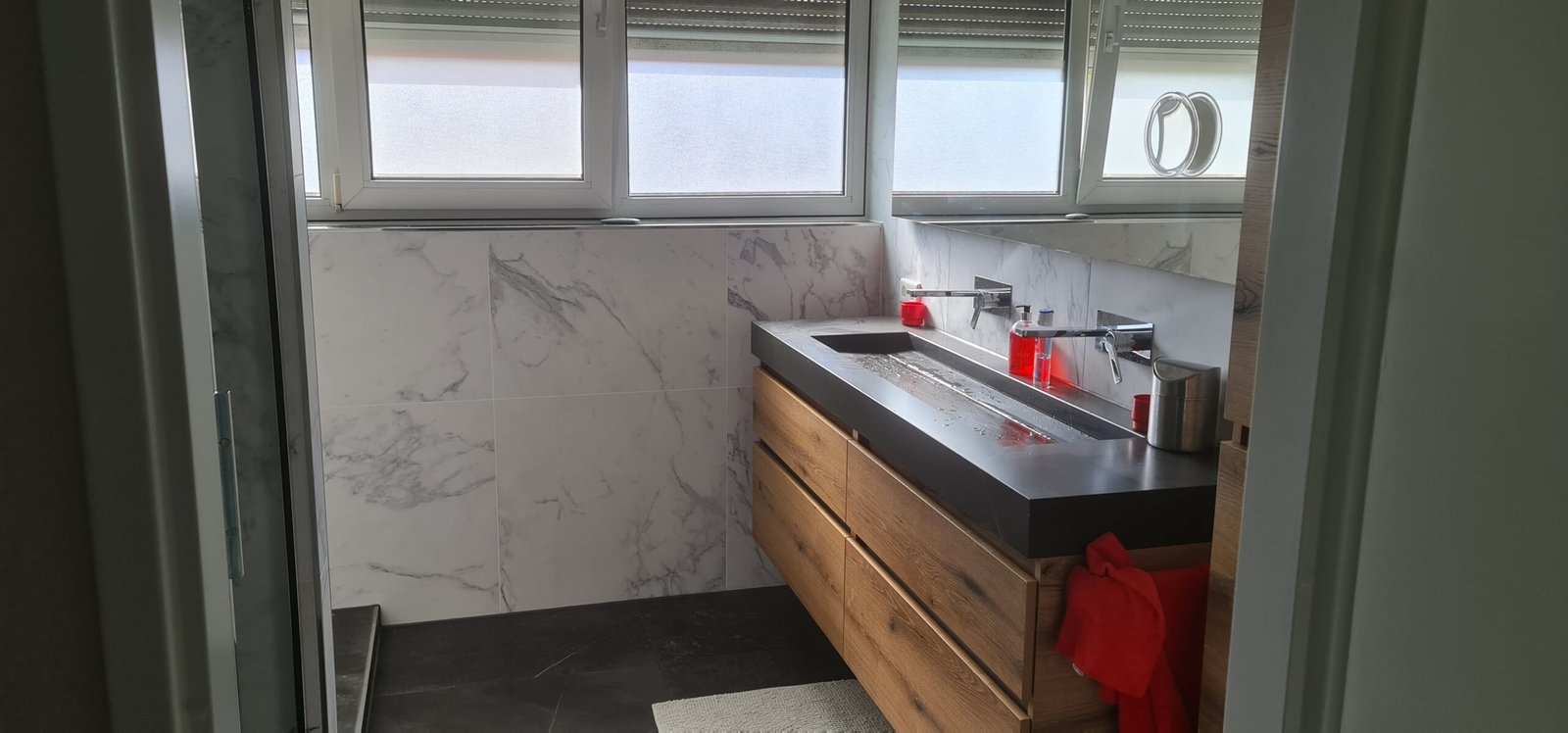 Modern zwevend badmeubel tegen een wand met grote marmerlook tegels en strakke RVS inbouwkranen. Gerealiseerd project in Groningen.